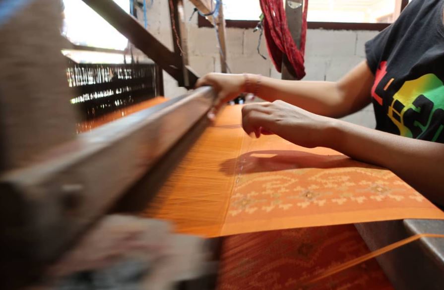 A weaver working on a new orange textile using a traditional loom.